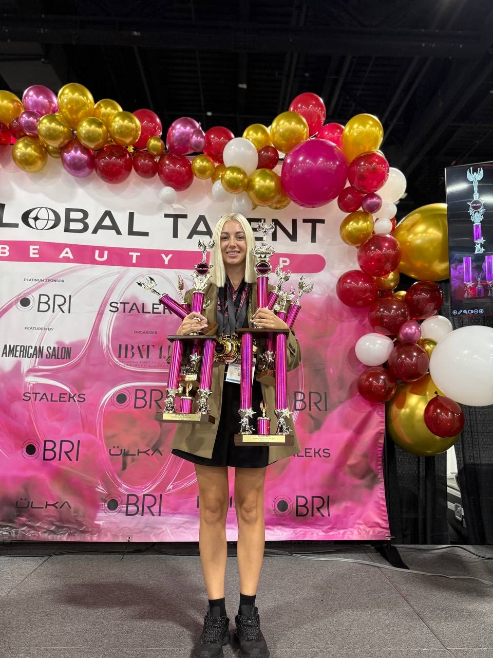 Kristina Strilets with trophies in front of the Global Talent Beauty Cup backdrop